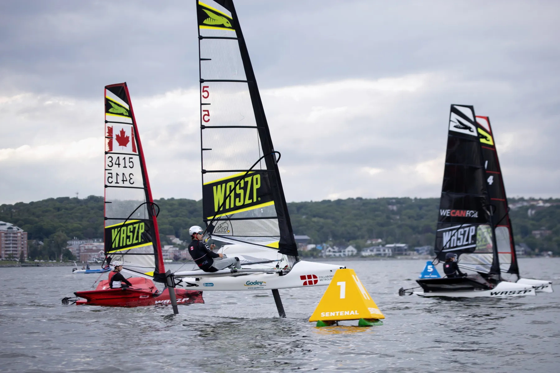 Three foiling dinghies at a yellow Sentenal with a second Sentenal behind