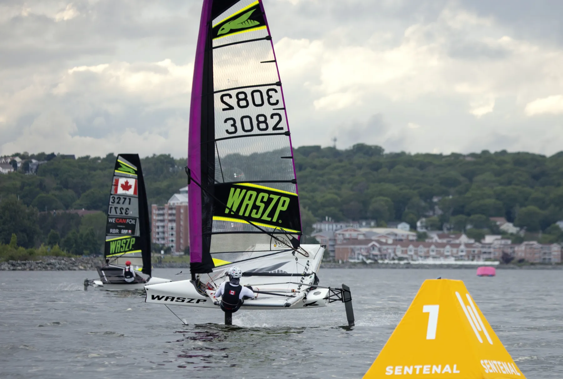 A yellow Sentenal on station with a foiling dinghy crossing behind