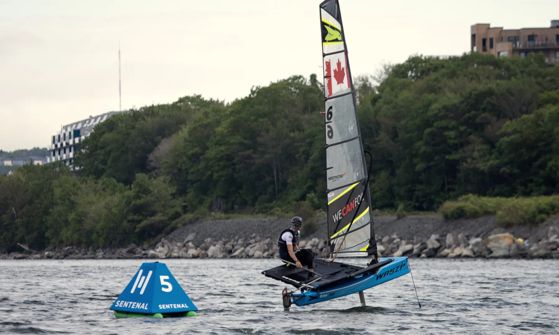 A foiling dinghy passing a blue Sentenal near the shore